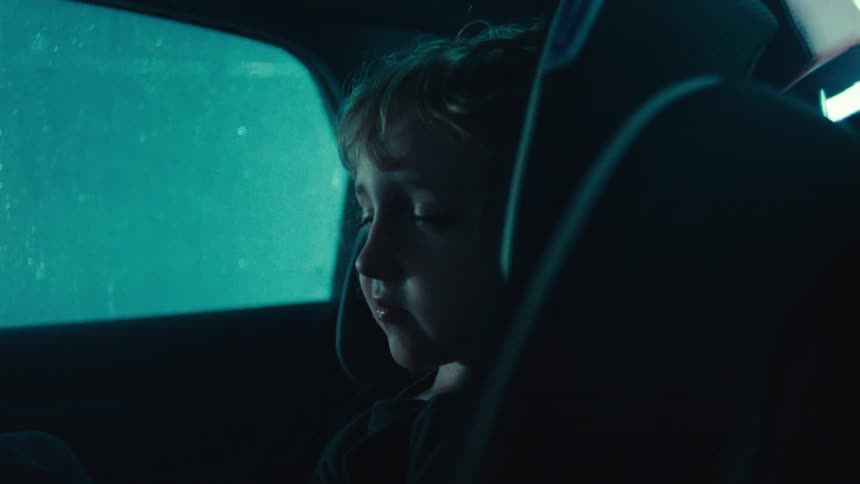 Child sleeping inside a car with rain outside