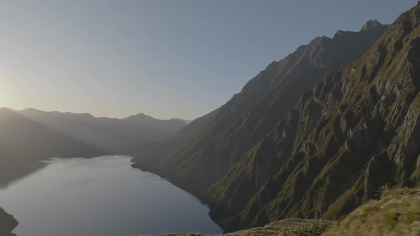 A long still lake fills a valley floor flanked by steep rugged mountains under a clear sky