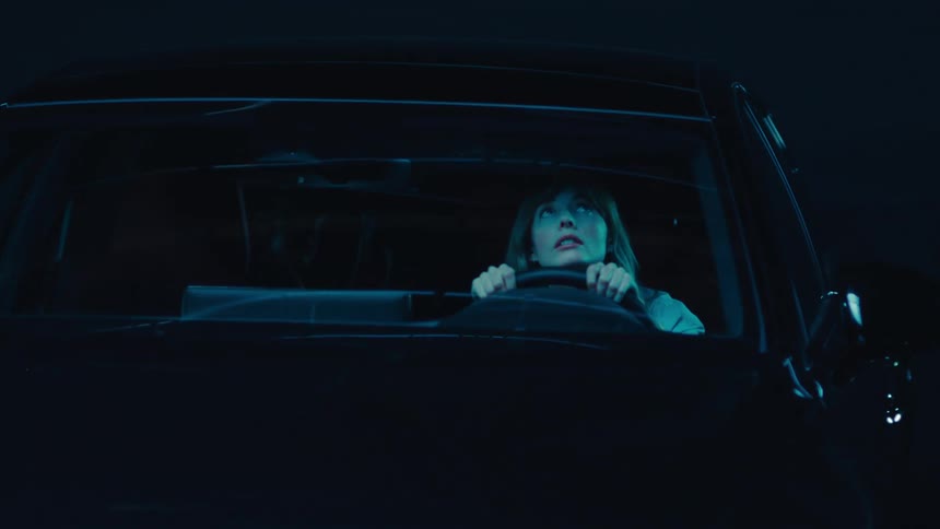 A woman sits in the drivers seat gazing upward through the windshield at night