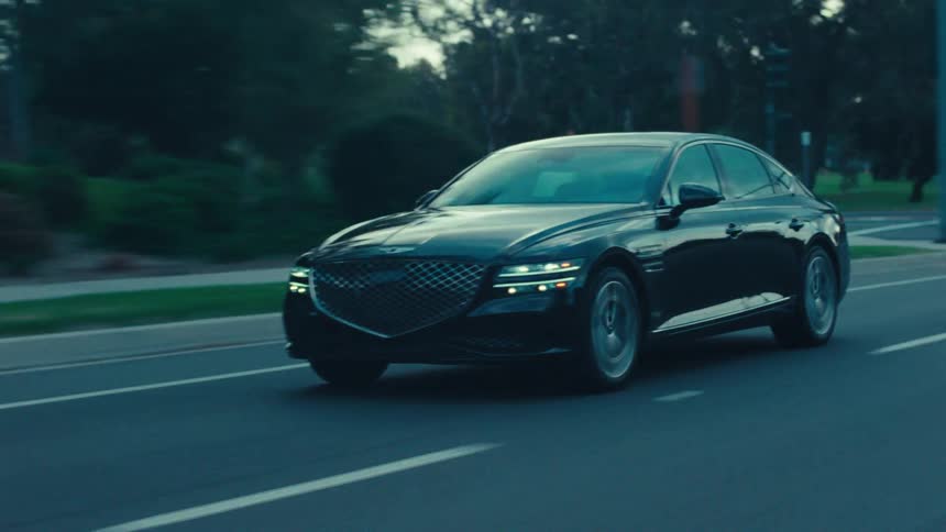 A black sedan travels along a road during dusk or dawn