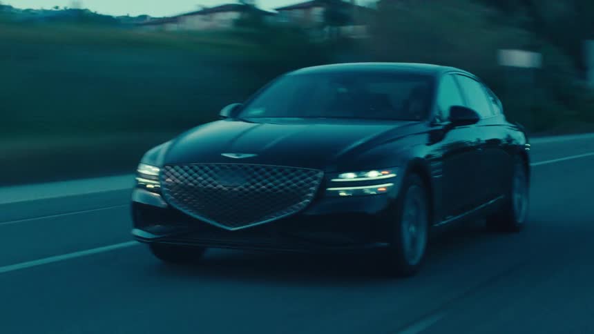 A black sedan travels along a road during dusk or dawn
