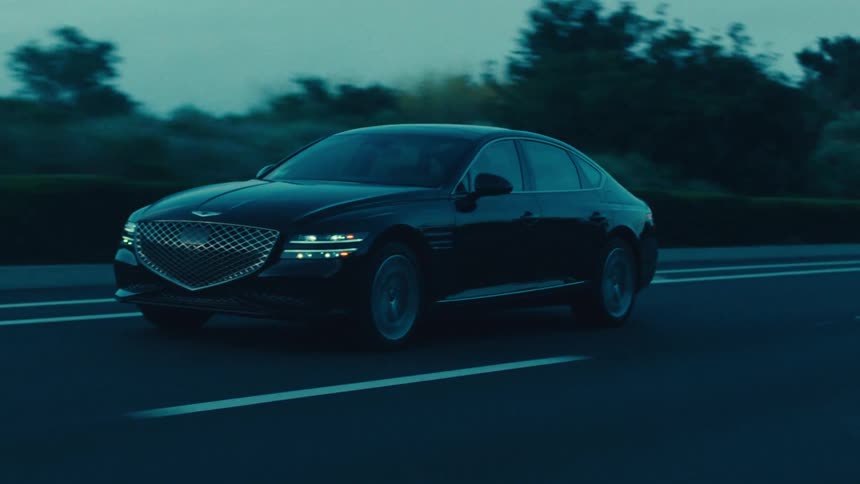 A black sedan drives along a rural highway at dusk