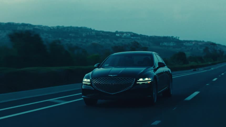 A black sedan drives along a rural highway at dusk