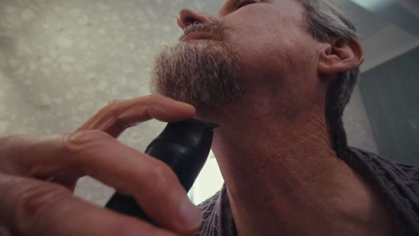 A person uses an electric razor to shave under their chin with the hand and neck area in focus