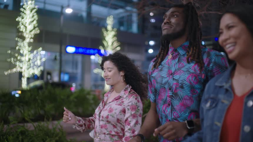 Man with two women walking on the sidewalk of a metropolis at night happily