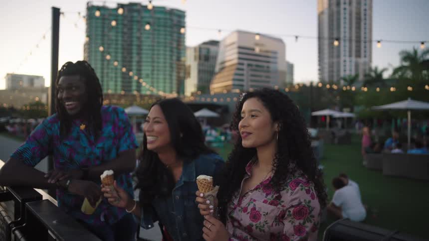 Three friends in an outdoor setting in the late afternoon with two eating ice cream and one having a glass of drink