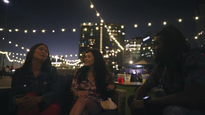 Friends sit at an outdoor table near the waterfront while enjoying the nightlife