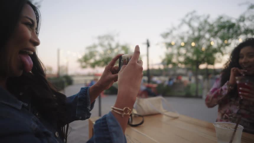Woman taking a photo of two happy friends sitting at a table outdoors