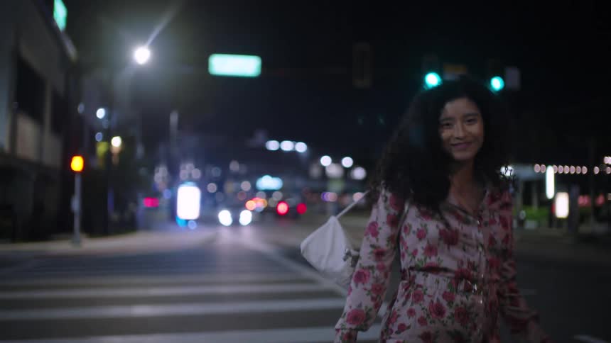 A woman is crossing the street at night