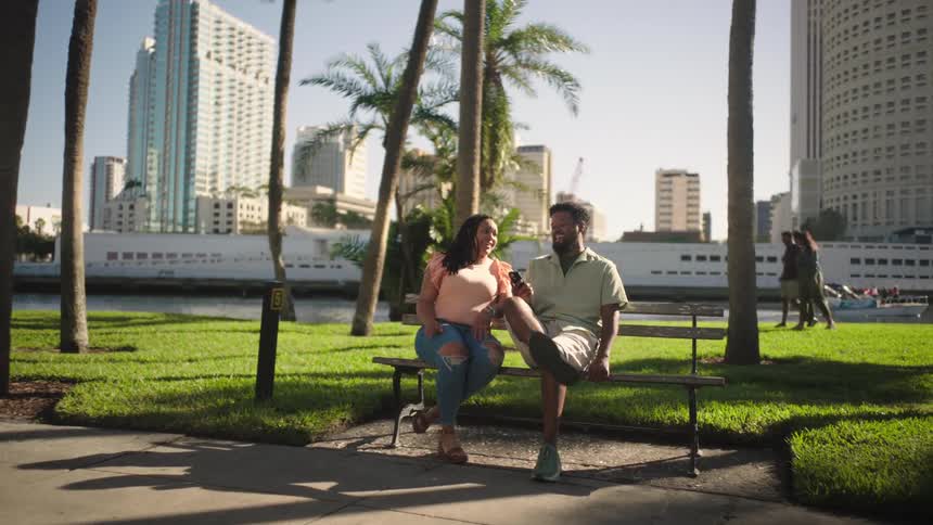 Woman and a man sitting on a bench in a square with palm trees and buildings in the background
