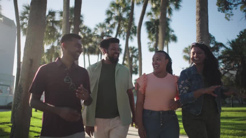 Group of four friends walking through a park talking happily
