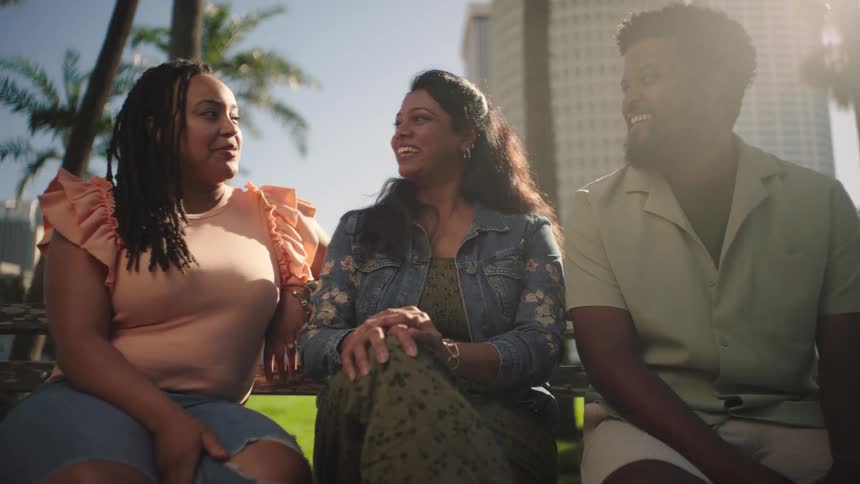 Two women and a man sitting on an outdoor bench having a relaxed conversation