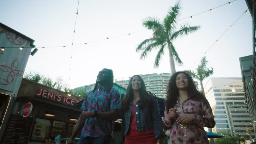 Man and two women walk outdoors near bars while happily chatting
