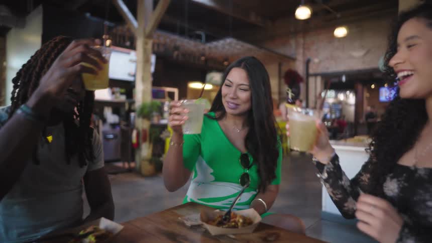 Three friends sitting at a bar toasting and drinking