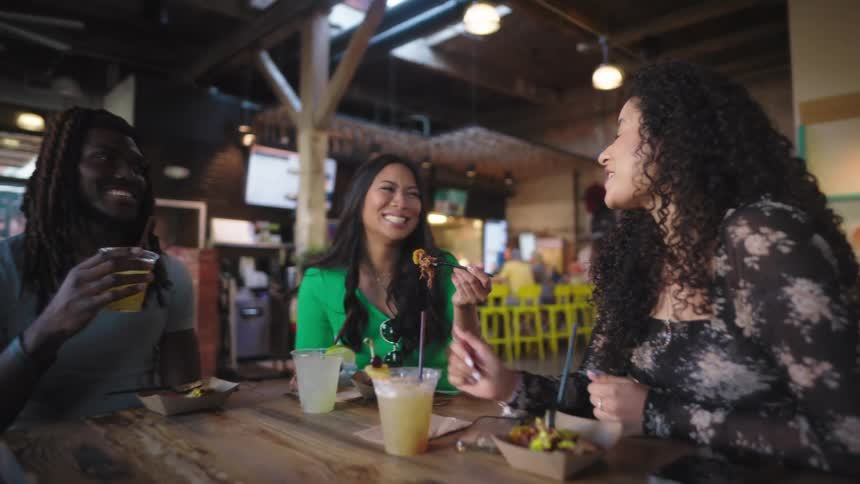 Friends sitting at a bar table talking while drinking and eating