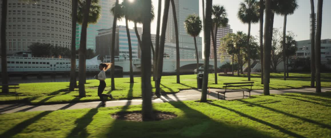 Female jogger runs through a riverside park across from downtown on a sunnysummer day