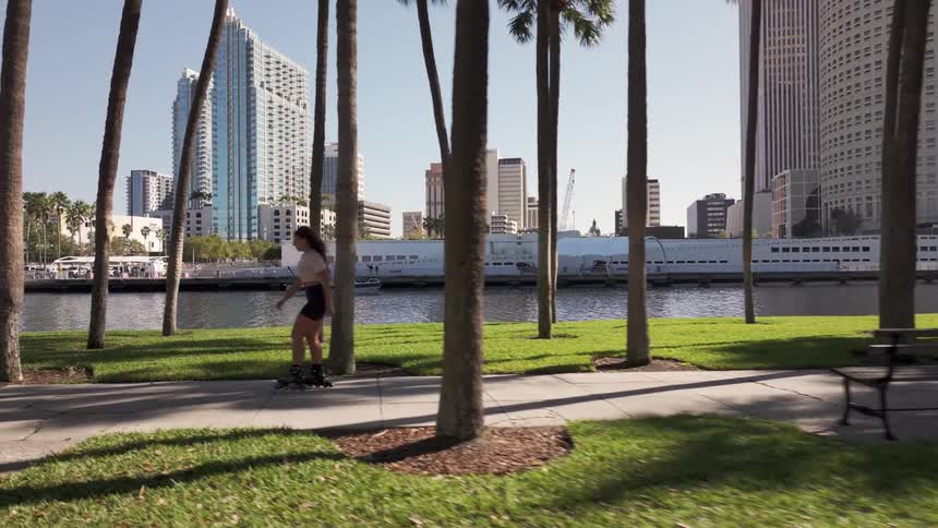 A young woman rollerblades on a sidewalk in the city along palm trees