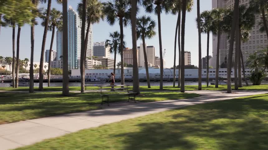 A teeenage girl rollerblades down a sidewalk in a park in the city
