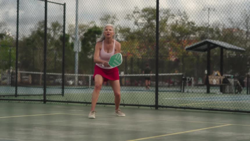Woman in red skirt on an outdoor court playing pickleball