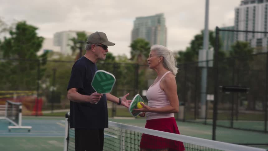 Couple on an outdoor court talking and holding tennis racket