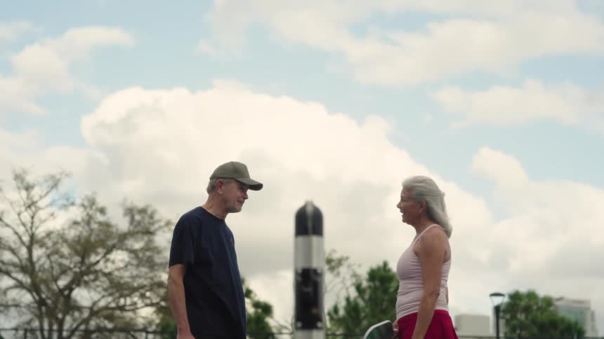 A man and woman playing pickleball talk by the net