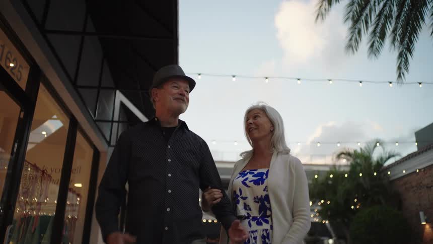 Elderly couple holding hands walking through an area with shops around
