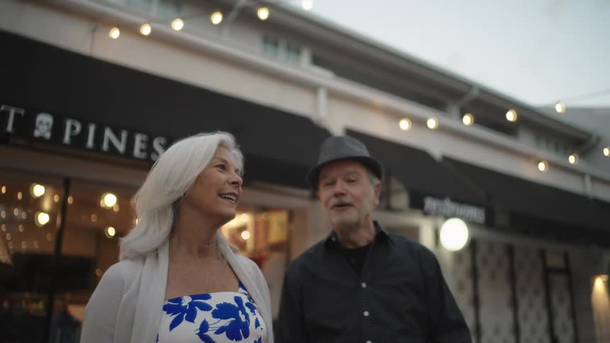 An elderly couple walk together and talk in a shopping plaza downtown