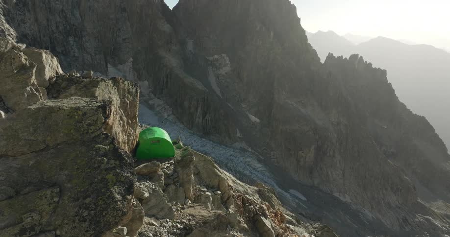 Isolated green tent is set up on rocks in rugged mountainous terrain