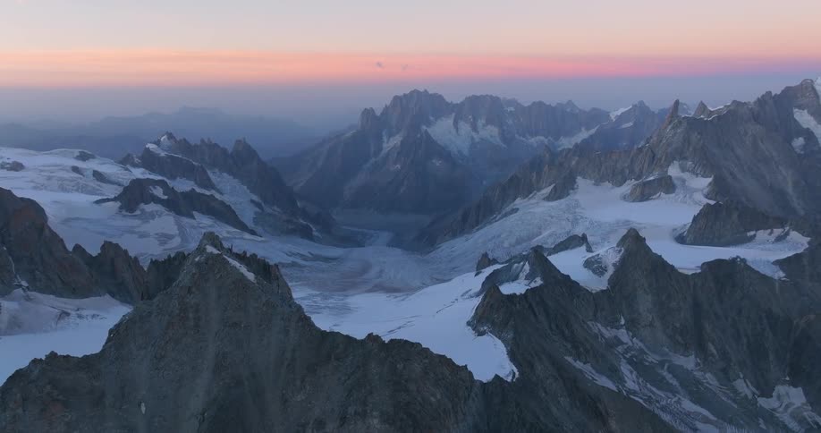 A breathtaking panoramic view of snow capped jagged mountains bathed in the soft hues of a pastel sunrise