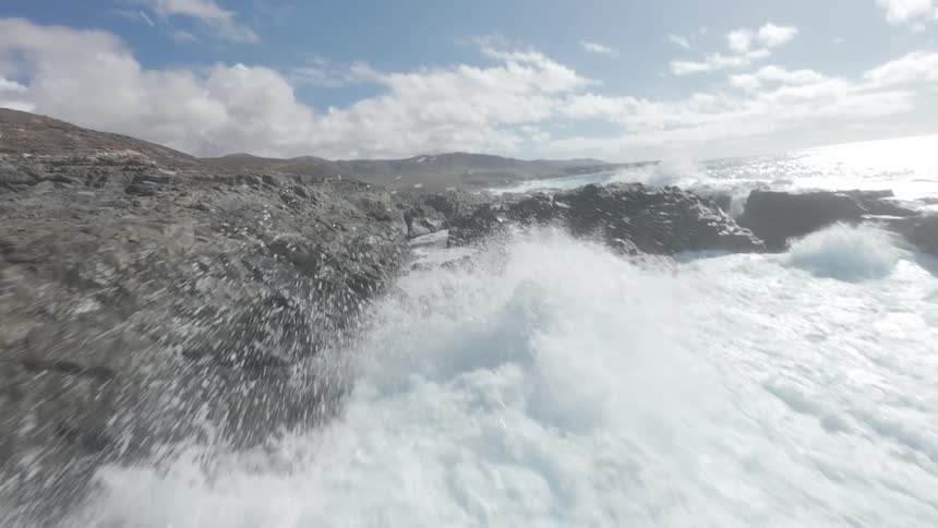 Aerial of ocean waves crashing against a rocky coastline