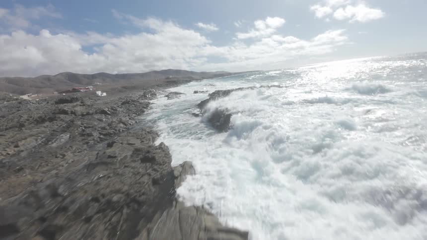 Aerial of ocean waves crashing into a rocky coastline on a partly cloudy day