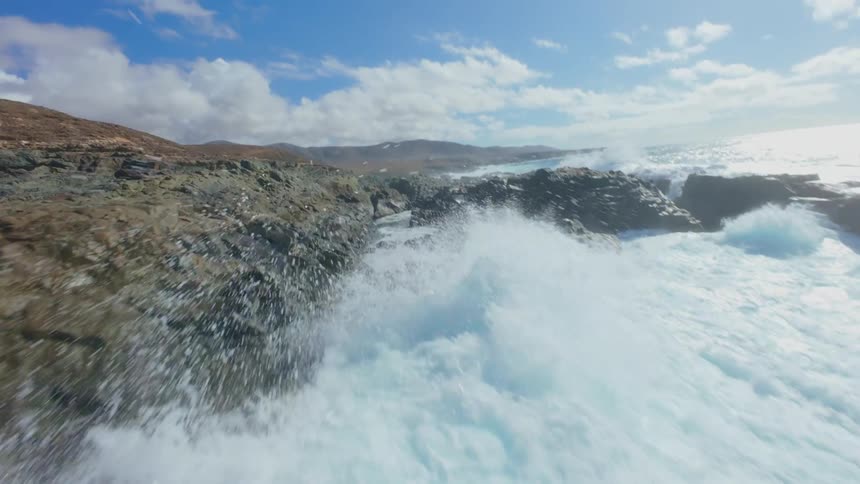 Waves crash powerfully against a rocky coastline creating turbulent turquoise water