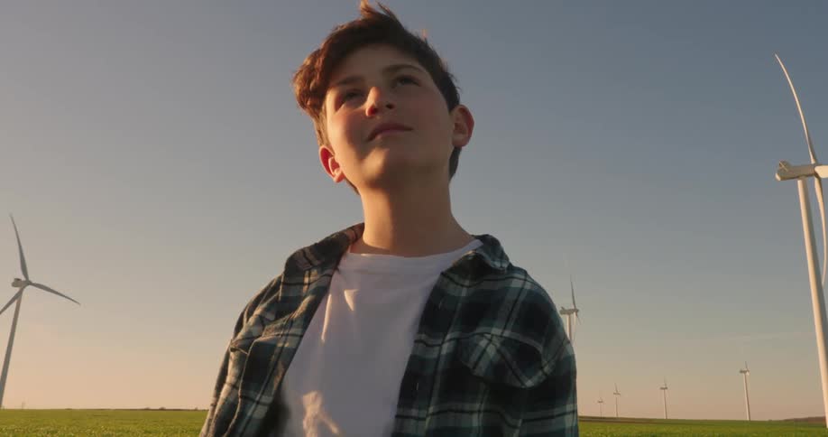 A boy stands contemplating something with windmills in the background