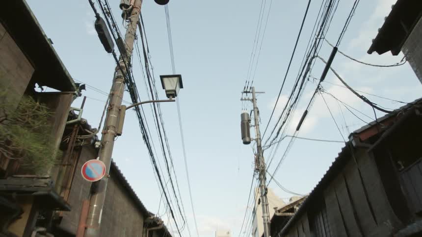 Buildings line a small street with power lines towering overhead