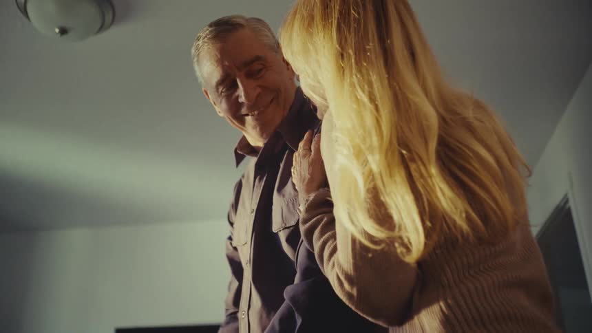 Woman walking into the room hugs a man as he folds clothes