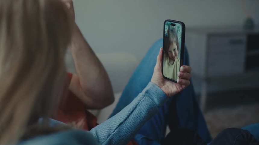 A couple of parents sit comfortably at home holding a phone while on a video call with their young daughter