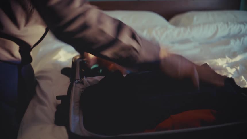 Man quickly putting clothes and closing suitcase on bed