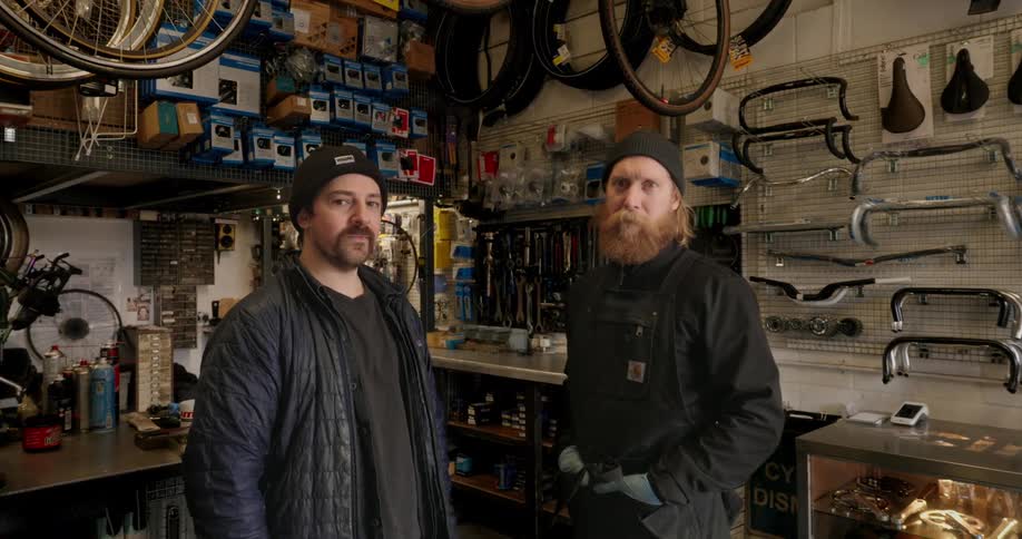 Two men inside a workshop with bicycle equipment