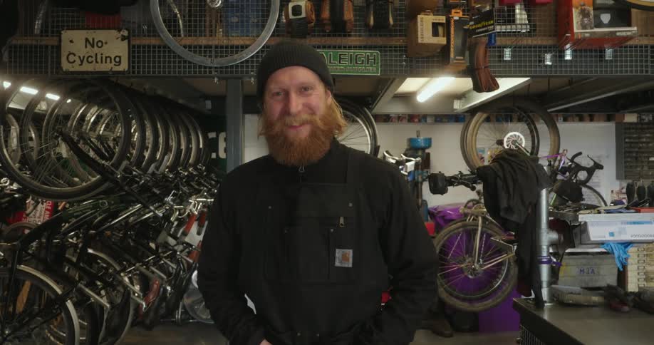 Redheaded man stands in a bicycle store and smiles