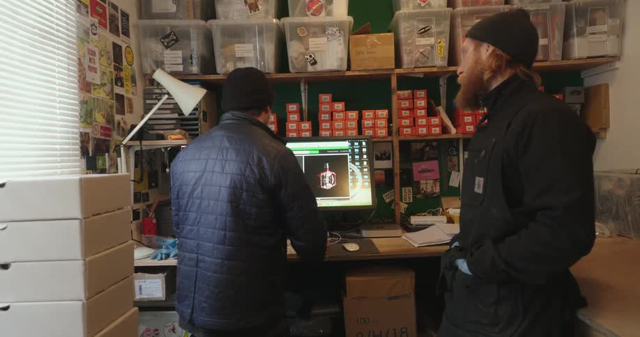 Two men interacting with a computer in a room with boxes