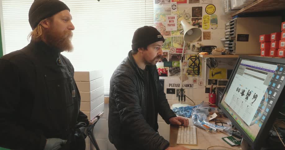 Two men interacting with a computer screen with bicycle parts