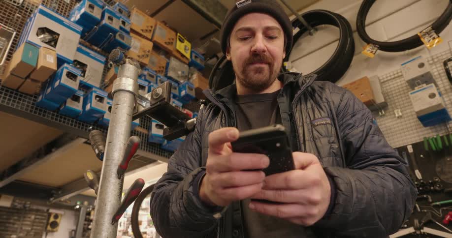 A man stands in a workshop and scrolls on his smartphone