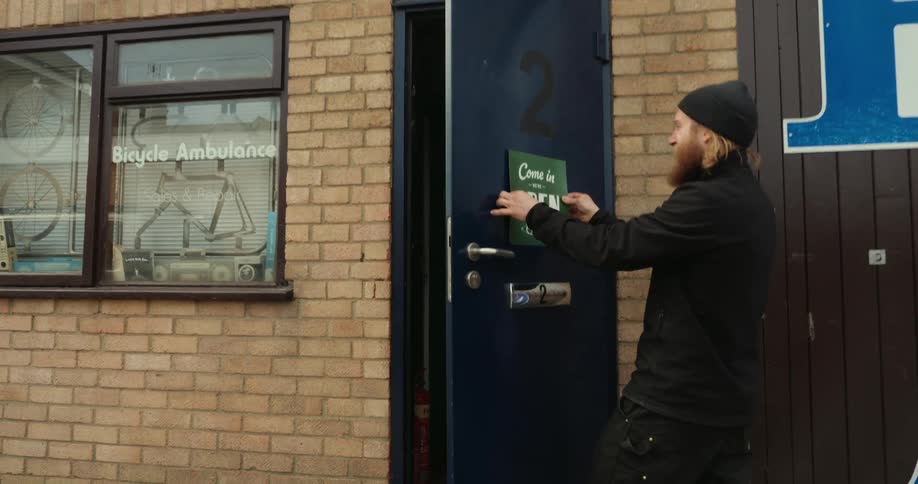 A man places a green come in open sign on the door of a bicycle repair shop