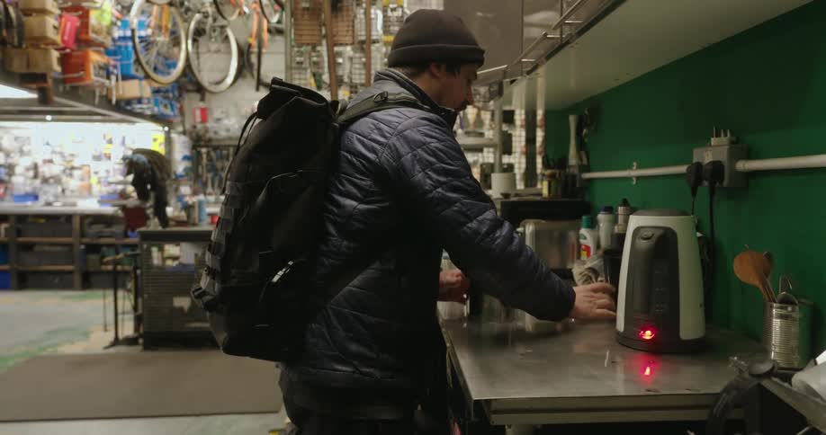 Man in a cap preparing a hot drink for himself inside a bicycle workshop