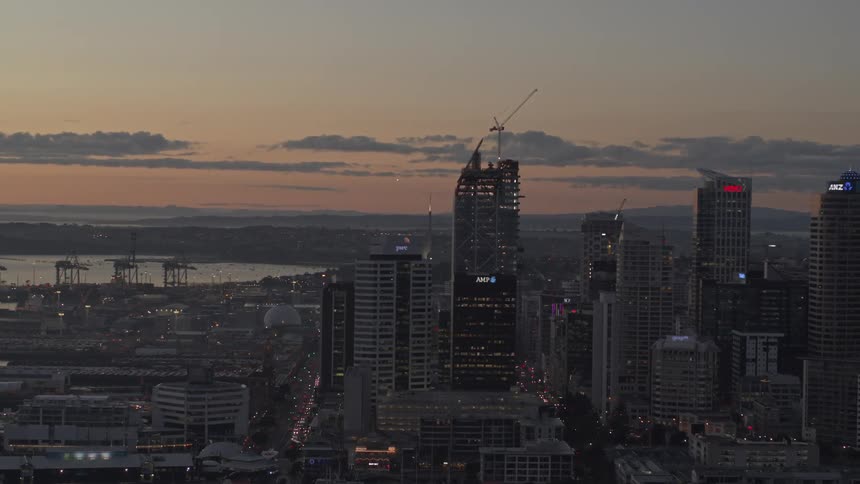 Construction crane stands on top of a skyscraper under construction near the waterfront against a red tinted sky