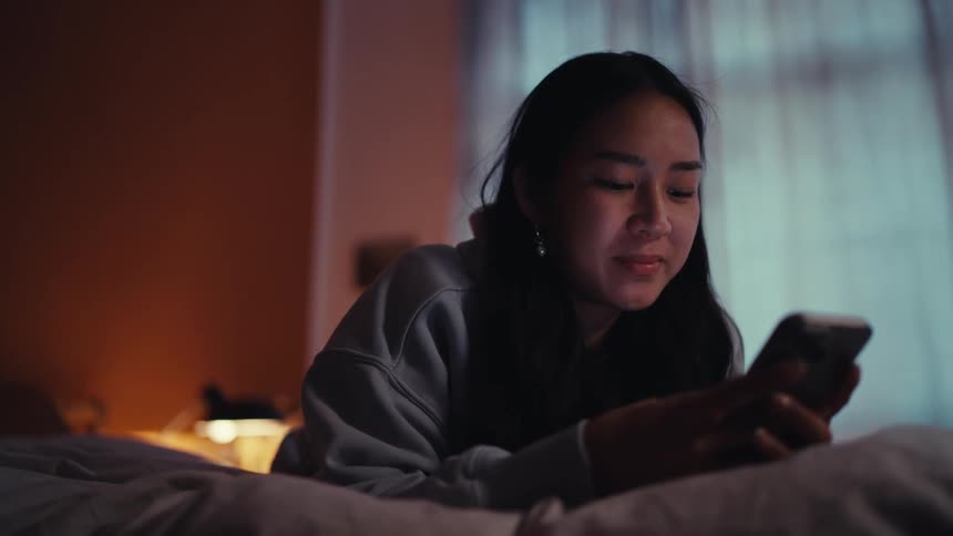 Teenage girl lying on her bed scrolls on her smartphone