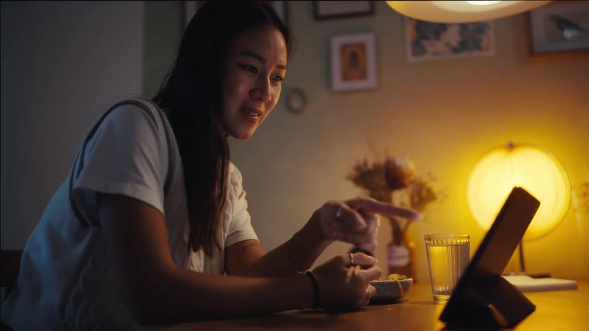 A young woman is sitting in front of a tablet with whom she is making a video call then she waves her hand