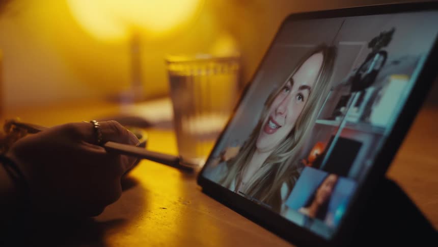 A woman is eating and talking with a friend on her tablet