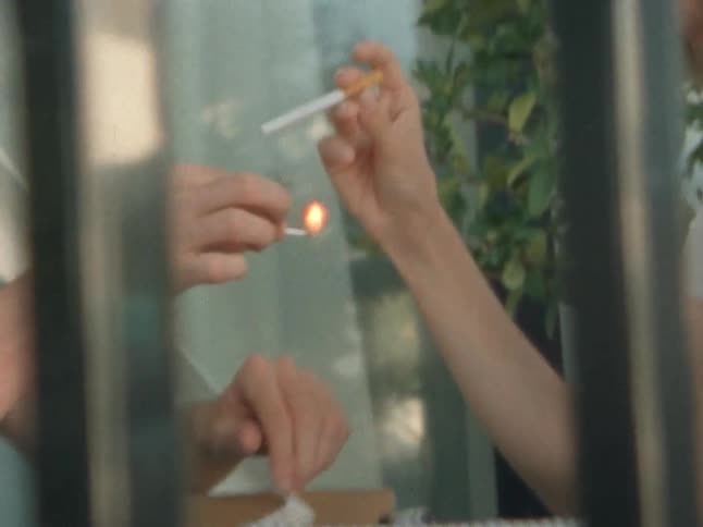 Person strikes a match to light the cigarette of a woman during the daytime