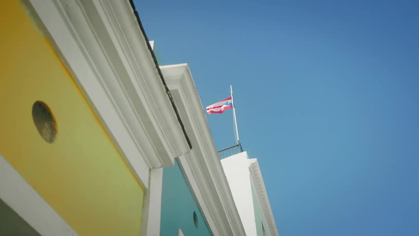 A colorful building with vibrant yellow and blue walls accented by white trim features a flagpole displaying the puerto rican flag against a clear blue sky